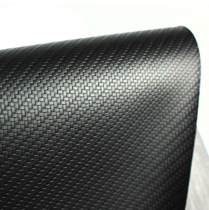 A close-up of a black carbon fiber textured material, showing a woven pattern and glossy finish, rolled over on a white background.